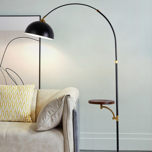 Modern black floor lamp with an arched design and integrated side table, placed beside a beige sofa in a contemporary living room setting.